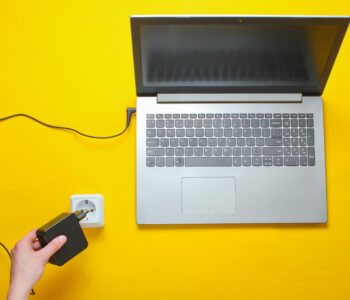 Laptop charger and electro outlet on a yellow background. The concept of electro addiction. Top view